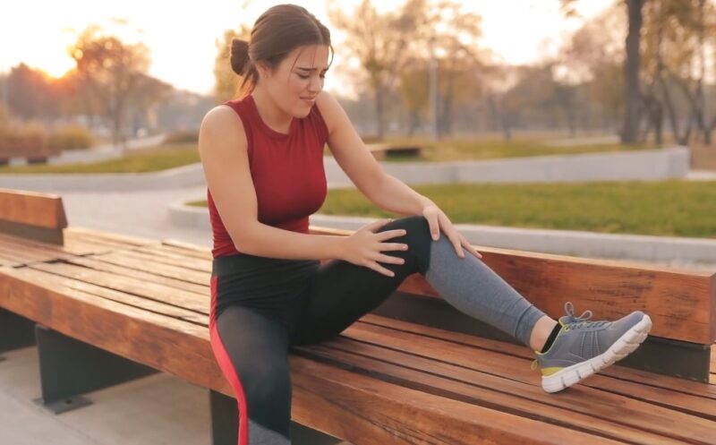 Woman experiencing knee pain, sitting on a park bench