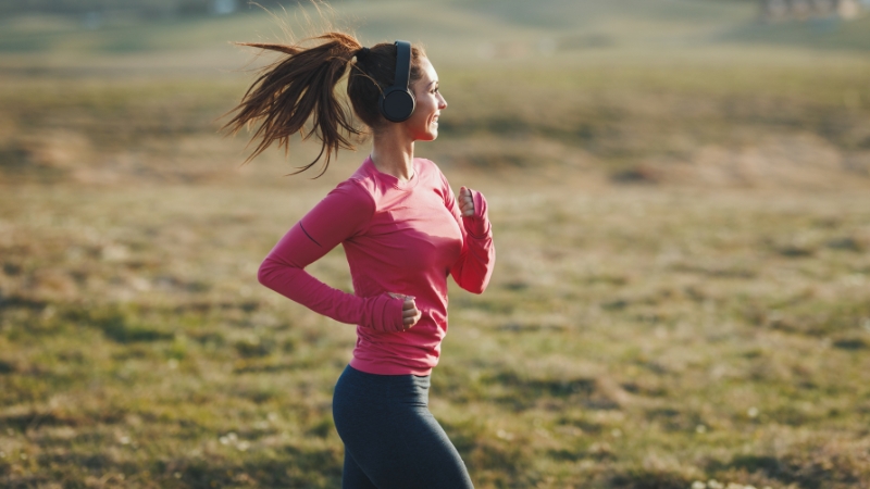 A Woman in A Pink Shirt and Headphones Jogging Outdoors, Showing Running Motivation