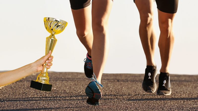 Two Runners on A Road with A Hand Holding a Golden Trophy in The Foreground