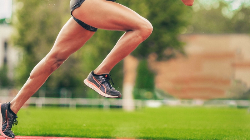 A Runner's Powerful Legs in Motion on A Track, Wearing Black Shorts and Running Shoes