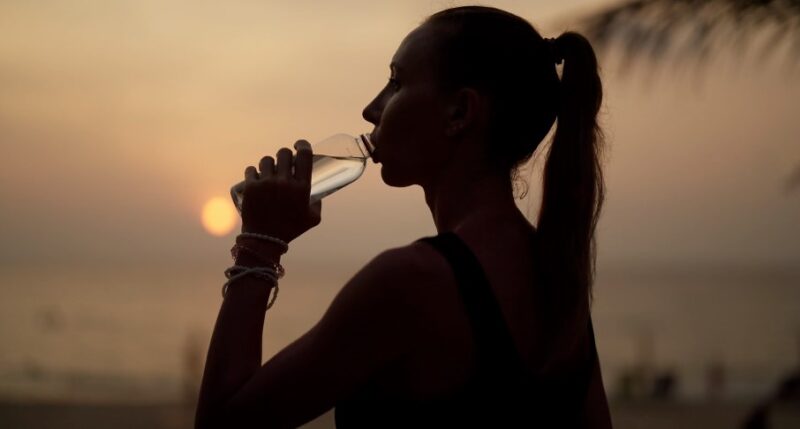 Silhouette of a woman drinking water at the beach at sunset