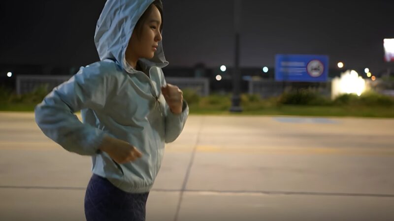 A young woman in a light blue jacket runs at night