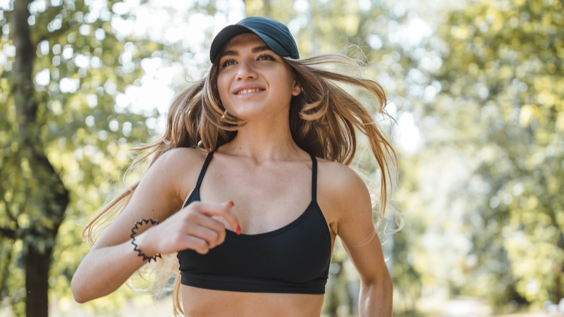 A Young Woman in A Black Sports Bra and Cap Jogging Outdoors