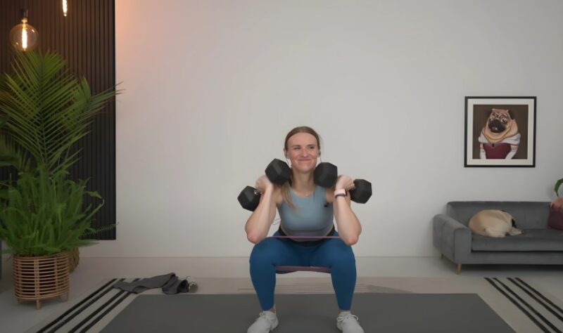 Woman performs a dumbbell squat with resistance band