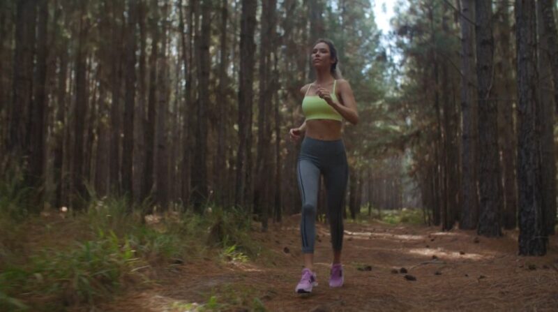 A woman runs through a pine forest trail