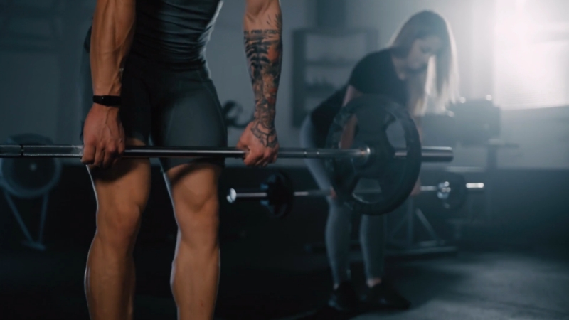 Two people performing deadlifts in the gym to strengthen their posterior chain for better running performance