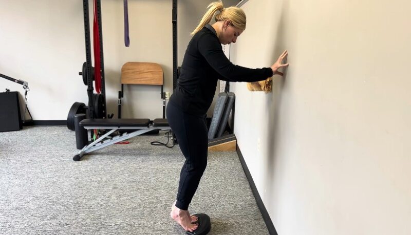 Woman performing a wall-assisted calf raise exercise