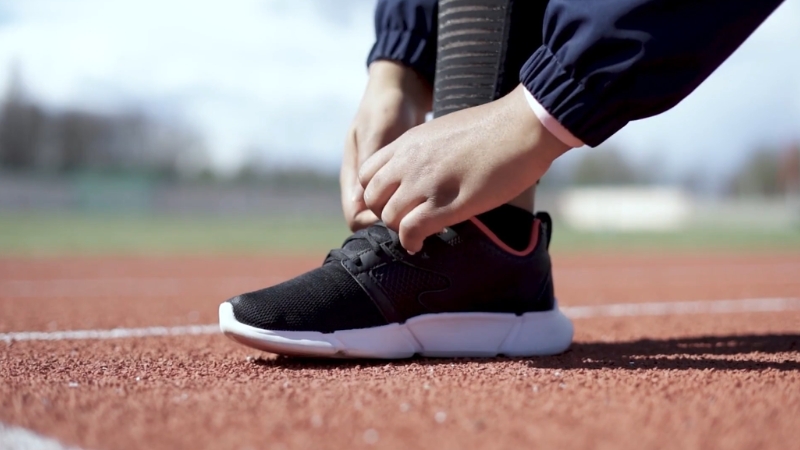 Person tying black running shoes on a track, showing proper footwear choice for managing Plantar Fasciitis