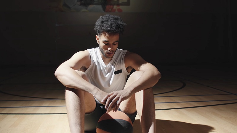 A basketball player sitting alone on the court, showing signs of emotional fatigue, an athlete struggling mentally