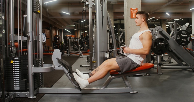 A man sitting on a gym machine performing seated cable rows in a weight training area