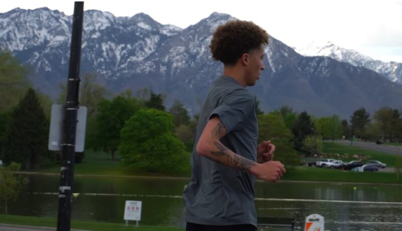 A man runs along a park path, the tranquil lake and distant mountains providing a peaceful setting