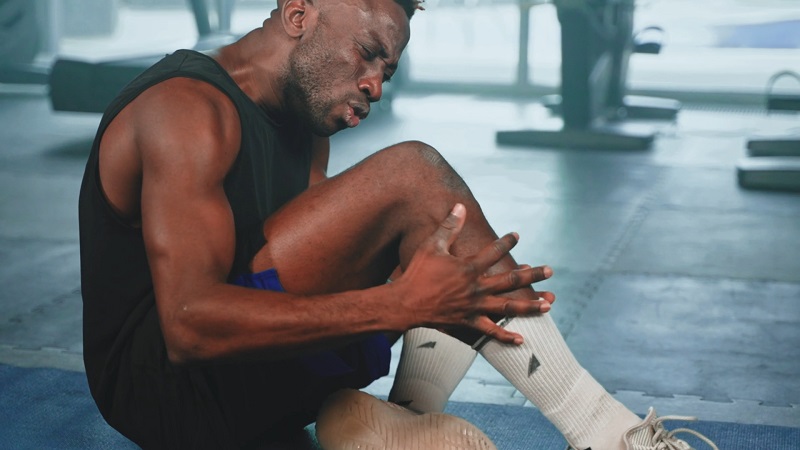 A man grimacing and holding his knee in pain after an apparent injury on the gym floor