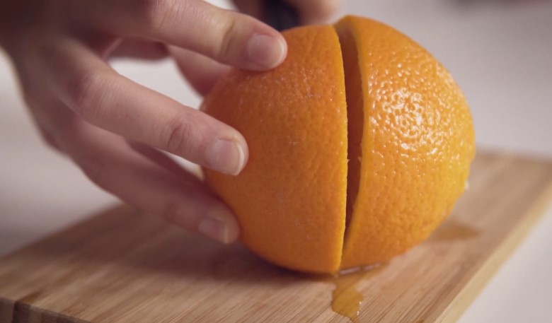 A close-up of a hand carefully cutting an orange
