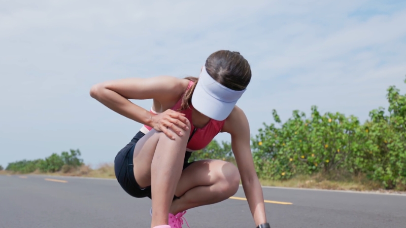 A runner experiencing knee pain while stopping to stretch during a run