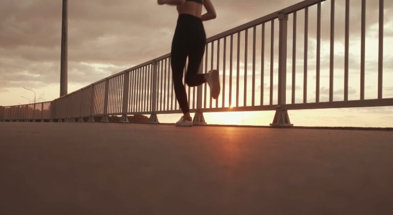 A runner strides across a bridge, the setting sun casting warm light on the pavement