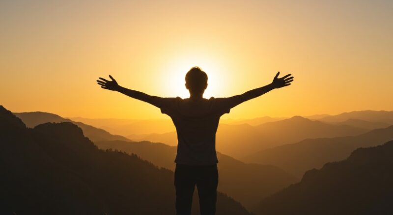 Silhouette of a person embracing the golden hour, arms outstretched against a backdrop of layered mountain ranges