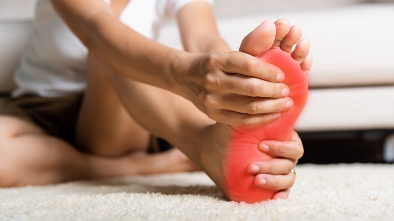 Person holding the bottom of their foot in pain, showing symptoms of Plantar Fasciitis