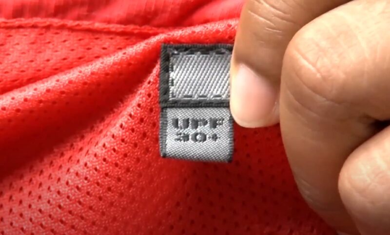 A close-up view of a red, breathable fabric with a gray care label
