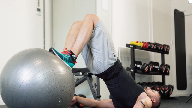 A person performing a hamstring curl using a stability ball to strengthen the posterior chain muscles