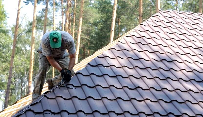 A man is installing a metal roof while standing on top of a building