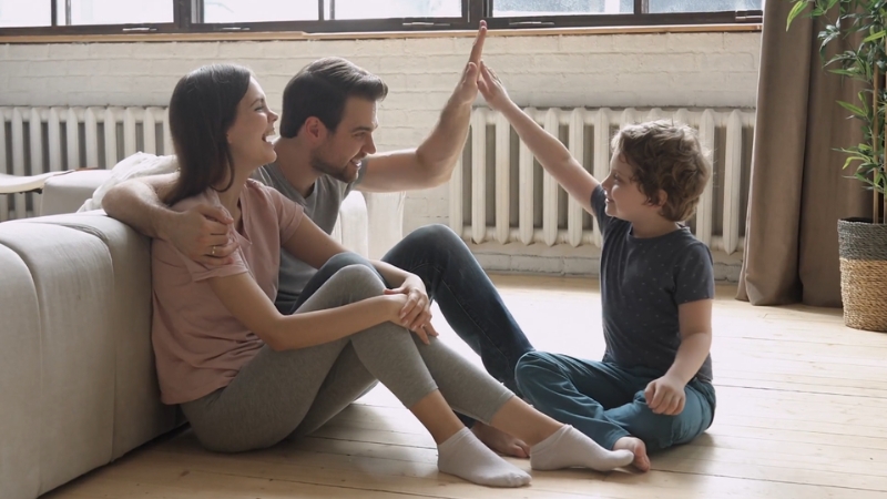 Parents sit on the floor with their child, sharing a high five while talking together