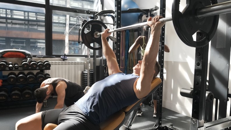 Man performing a barbell bench press in a well-equipped gym