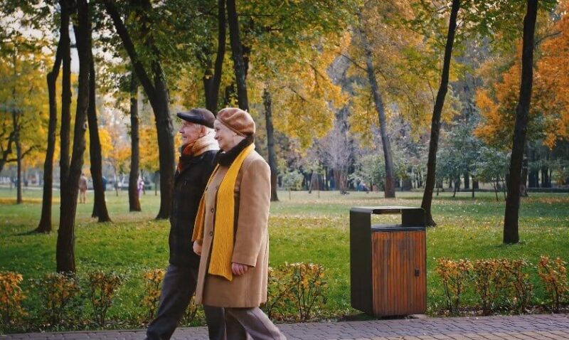 An elderly couple enjoys a leisurely walk through a park