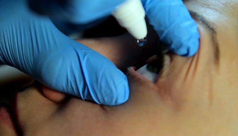 A gloved hand carefully administers eye drops