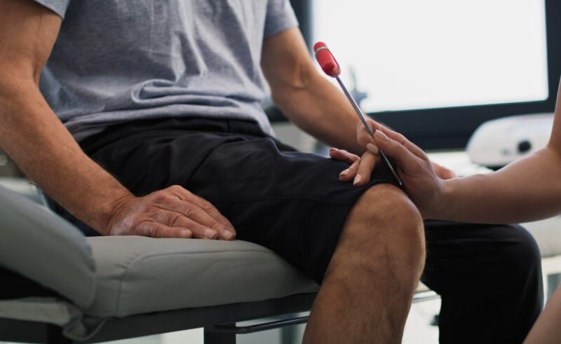 A physical therapist assesses the patient's knee using a reflex hammer