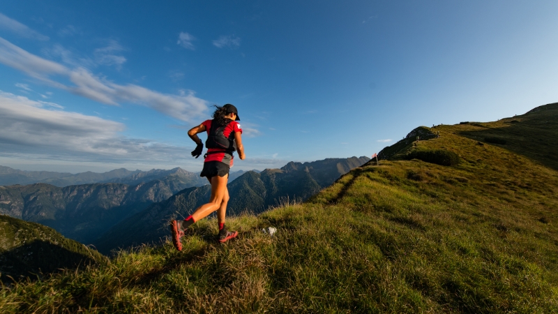 A woman runs uphill on a mountain trail during a clear day, showcasing the intensity of high altitude running