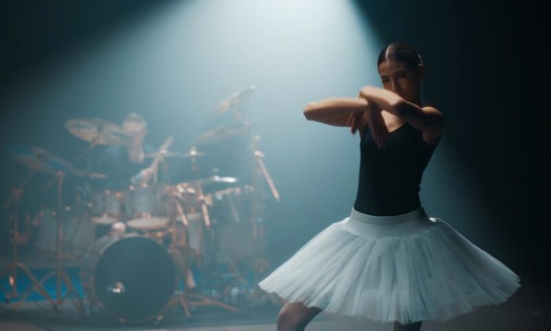 A ballerina gracefully moves amidst a backdrop of a live drum performance