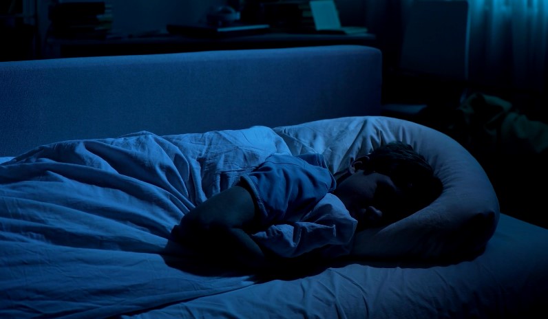 A person peacefully sleeping in a bed illuminated by soft blue light