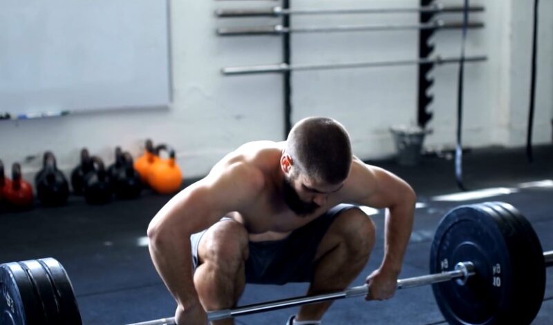 A man squats with a barbell on his shoulders in a gym