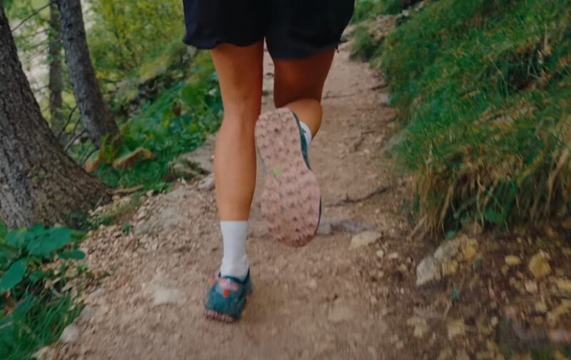 A person running on a dirt trail surrounded by trees in a lush green forest