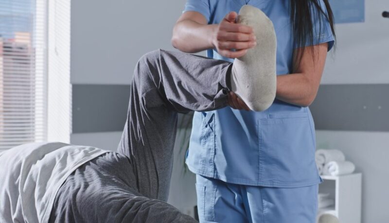 Physical therapy session in progress. A therapist assists a patient with leg stretching