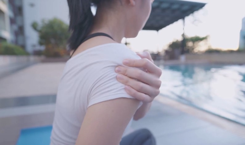 A woman gently massages her shoulder, likely experiencing discomfort