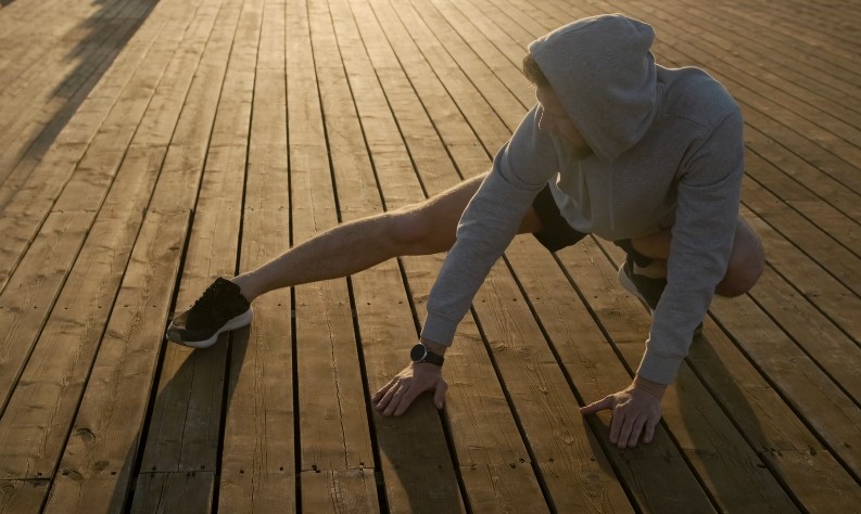 Man stretching on a wooden boardwalk, sunlight highlighting the planks