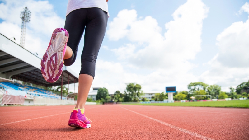A runner's legs are seen from behind on a track, with one foot lifted in motion, indicating a return to running