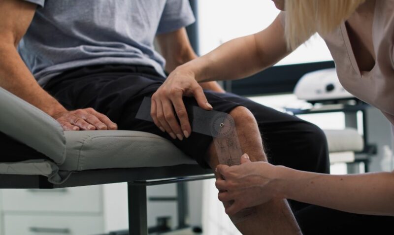 A physical therapist measures the knee's range of motion using a specialized goniometer