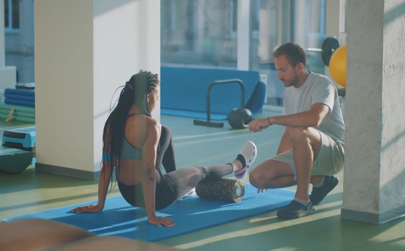 A woman receives focused physical therapy, her leg supported by a massage roller