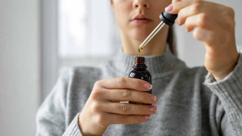 A woman holds a dropper bottle of CBD oil, preparing to use it for muscle inflammation relief