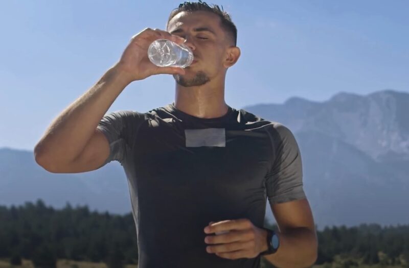 Thirsty athlete takes a refreshing drink of water amidst a scenic mountain backdrop