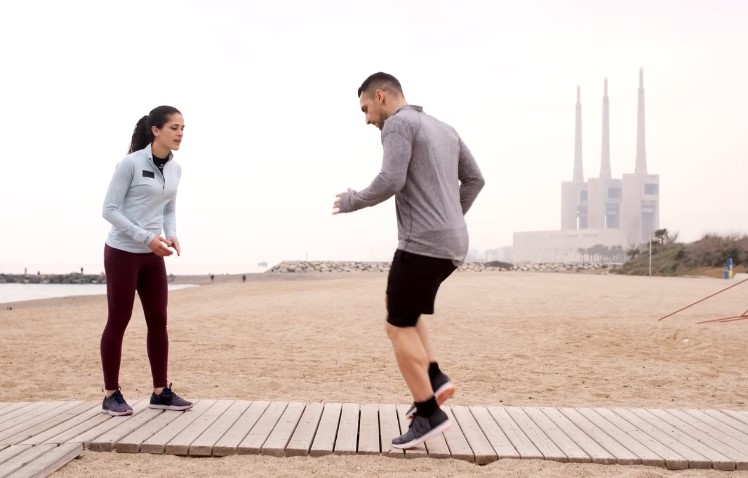 A personal trainer guides a client through dynamic exercises on a beach boardwalk
