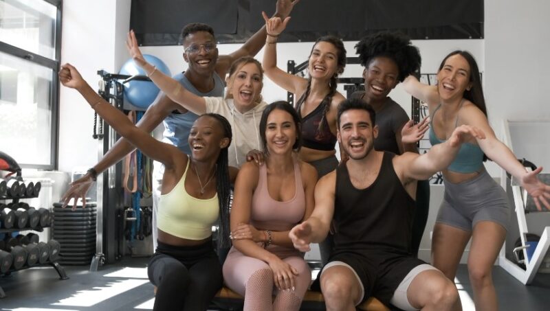 A diverse group of friends celebrates a successful workout session in a vibrant gym