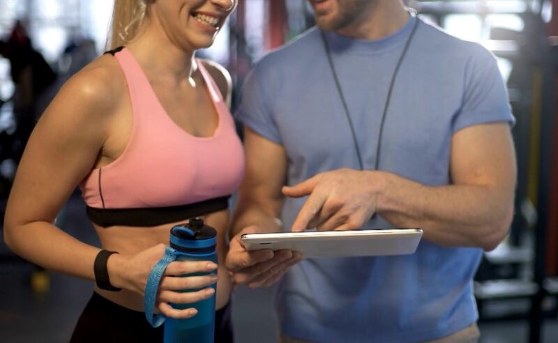 A trainer and client review workout progress on a tablet in a gym