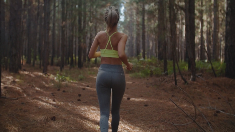 A woman runs through a forest trail in workout clothes as she builds endurance and tracks how many miles to run weekly
