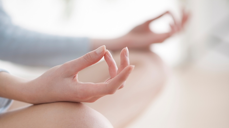 A person sits cross-legged with hands in a meditation pose, using mind-body techniques to ease pain