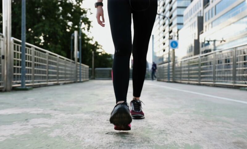 A person walks purposefully along a city bridge, focused on their stride