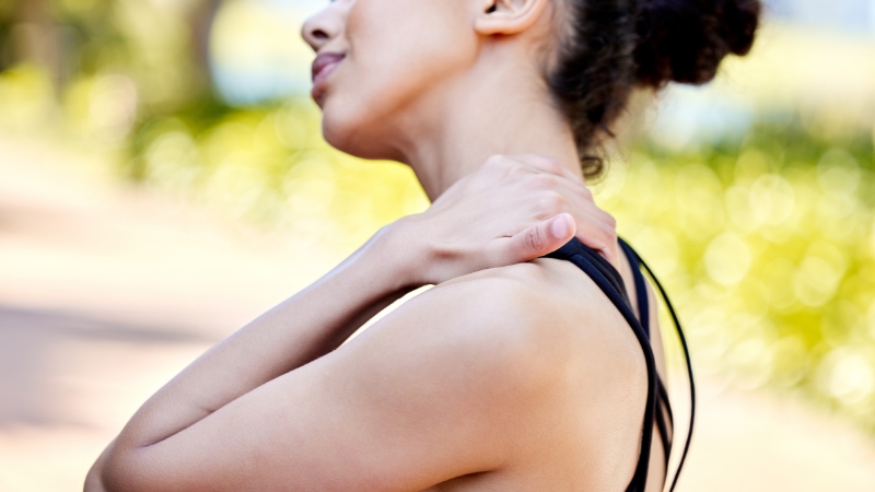 A woman holds her shoulder outdoors, showing muscle inflammation discomfort after exercise