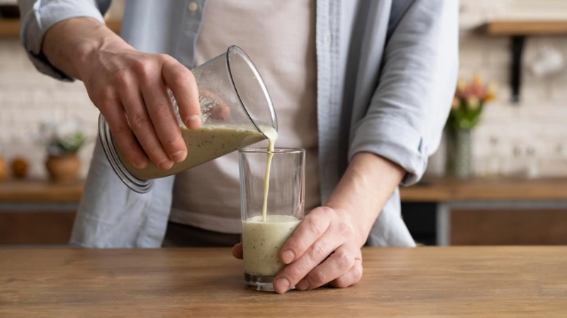 A person pours a green smoothie into a glass on a wooden kitchen counter, preparing a healthy pre-race breakfast drink